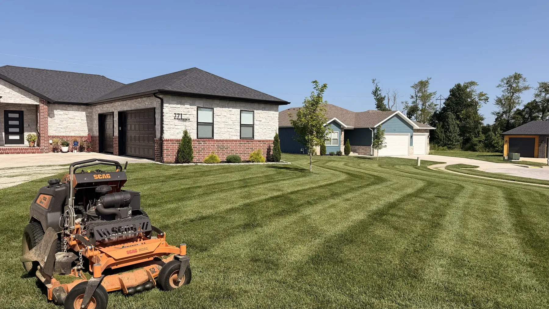 Pebble Creek mower beside a freshly striped lawn, with landscaping also completed by our team